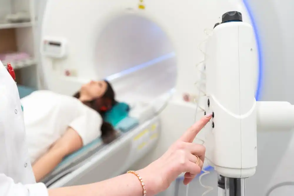 Patient lying on a hospital bed for an MRI scan while a technician presses the control panel on the MRI machine.