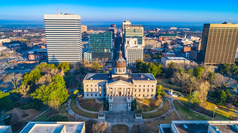 An aerial view shows the South Carolina State House surrounded by downtown Columbia buildings.