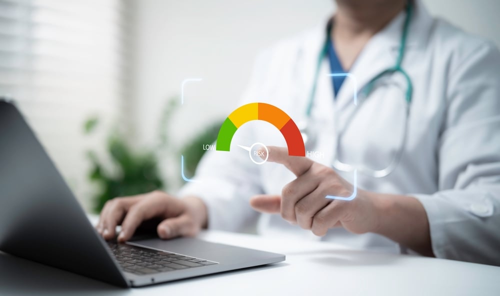 Doctor types on a laptop while pointing to a digital gauge showing risk from low to high