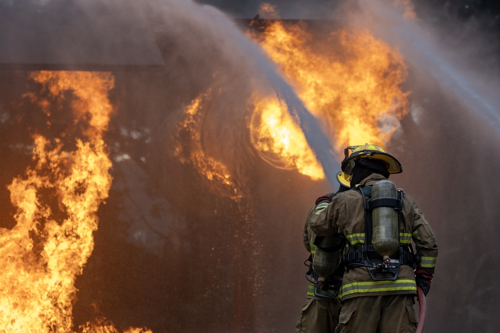 Firefighter Cancer Screening in Charleston: What Scans to Get and When 2 Firefighter in full turnout gear with air tank spraying a large wall of fire with a hose.