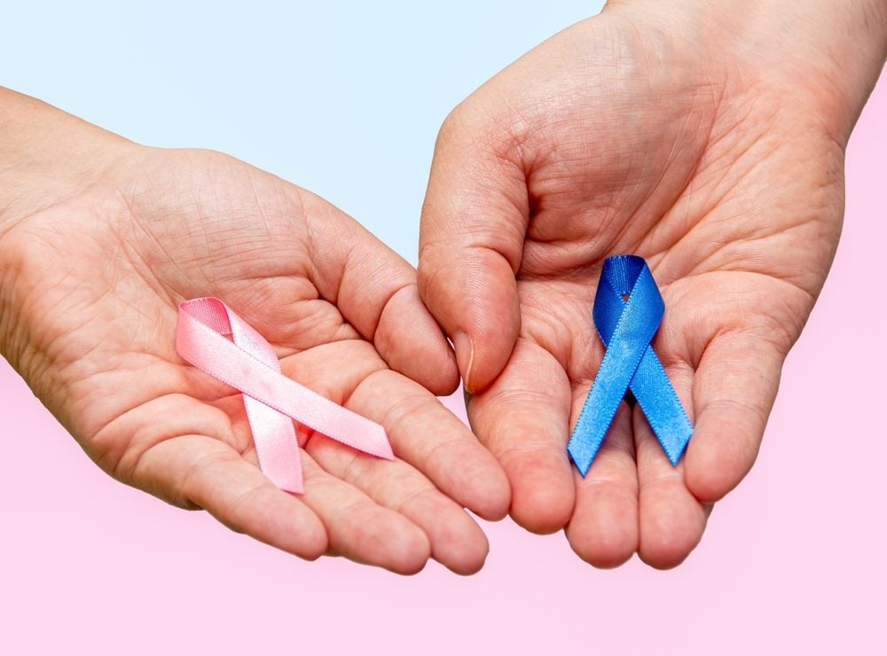 Two hands hold a pink ribbon and a blue ribbon for breast and prostate cancer awareness.
