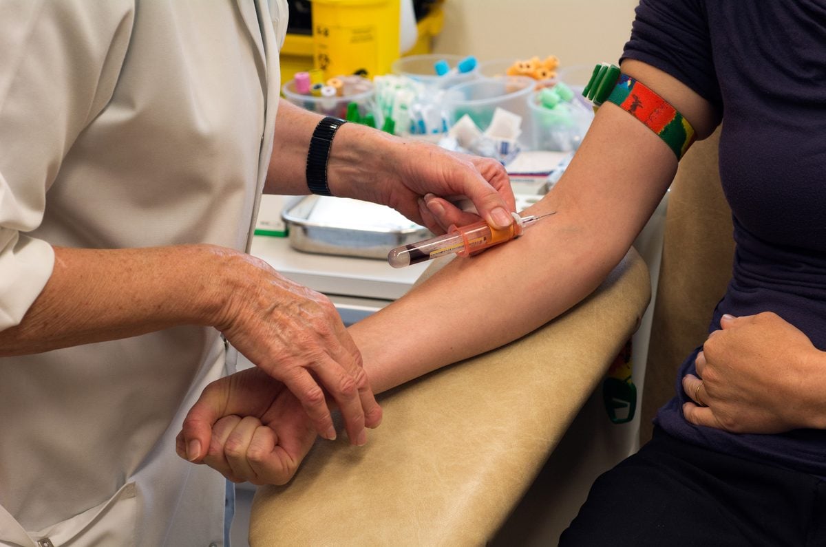 A nurse inserts a needle into a young woman's arm to draw a blood sample.
