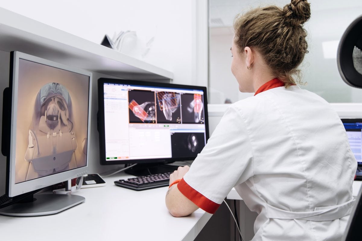 A radiologist viewed from behind studies whole-body MRI images displayed on two computer monitors.