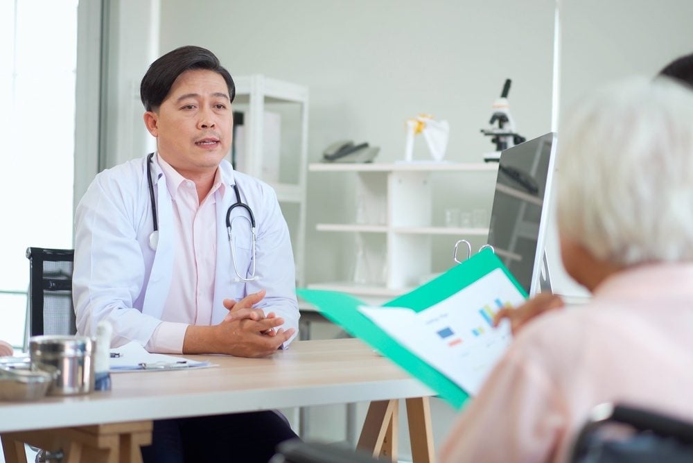 Doctor in a white coat talks with an older woman and her adult daughter during a visit