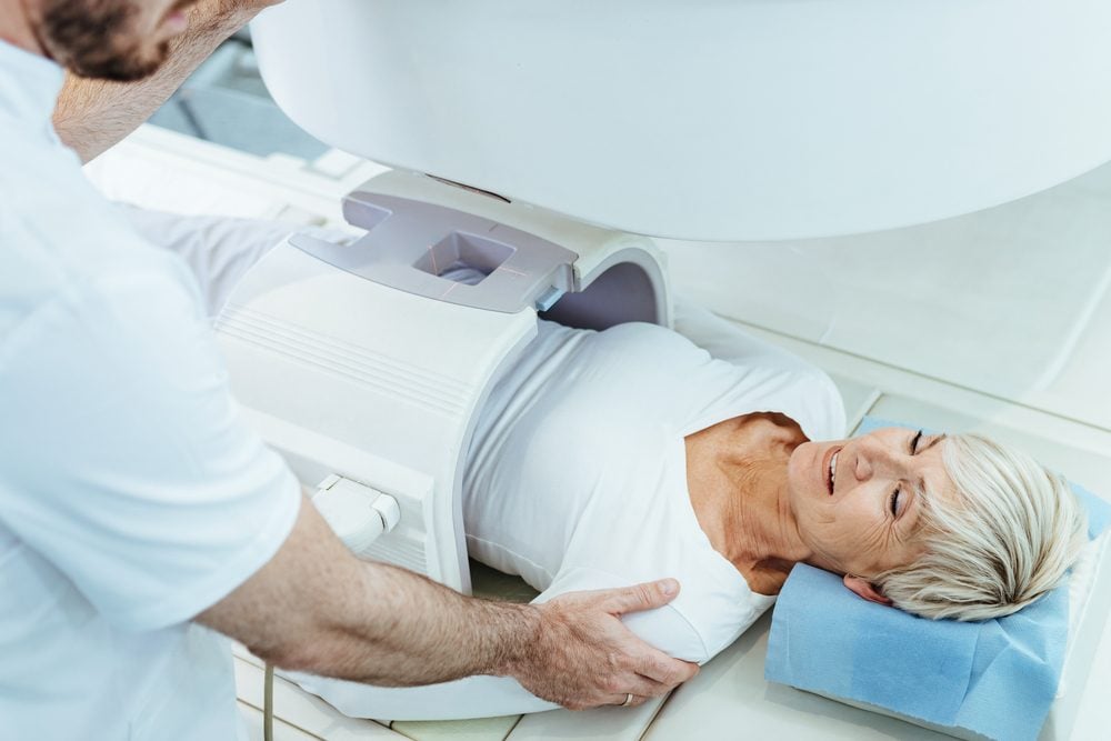 A technologist adjusts the MRI table while a smiling woman lies ready for her scan.